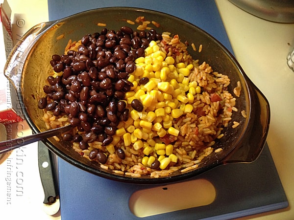 A bowl of Spanish rice with black beans and corn on top.