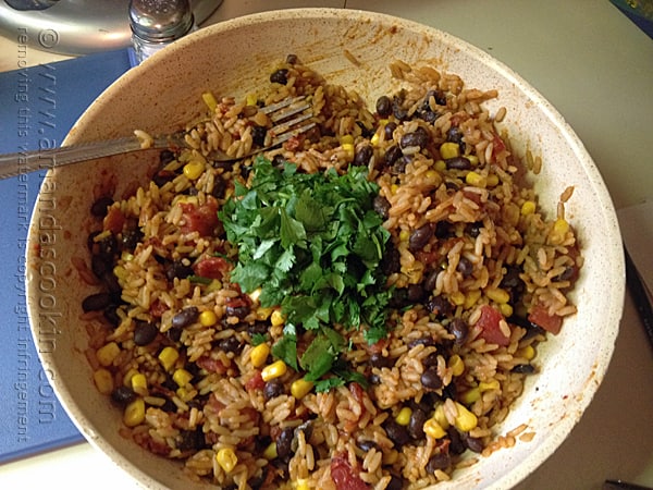 A bowl of Spanish rice with black beans, corn and cilantro on top.
