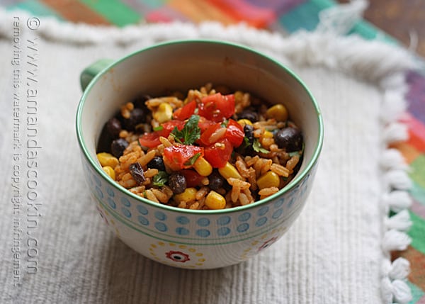 A close up photo of Spanish rice with black beans and corn in a teal and white bowl.