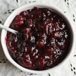 An overhead photo of whole berry cranberry sauce in a white bowl with a spoon.