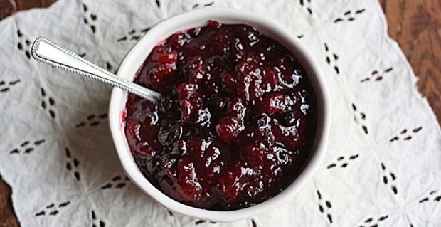An overhead photo of whole berry cranberry sauce in a white bowl with a spoon.