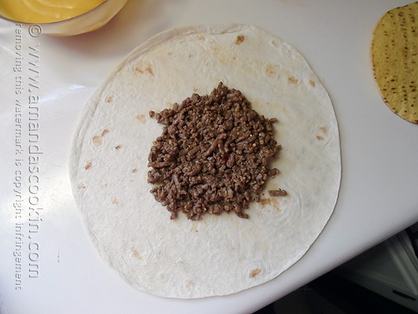 An overhead photo of a tortilla with cooked ground beef on top.