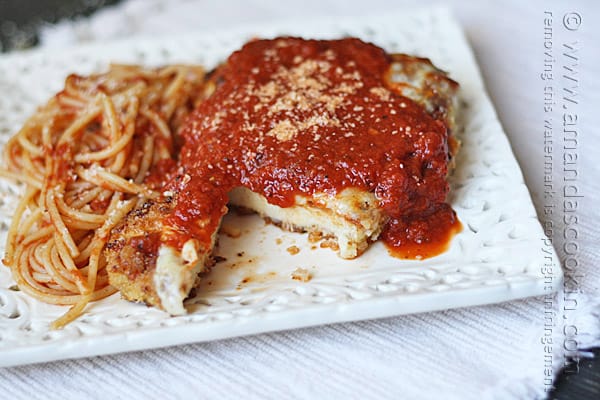 A photo of chicken parmesan on a white decorative plate with a slice missing.