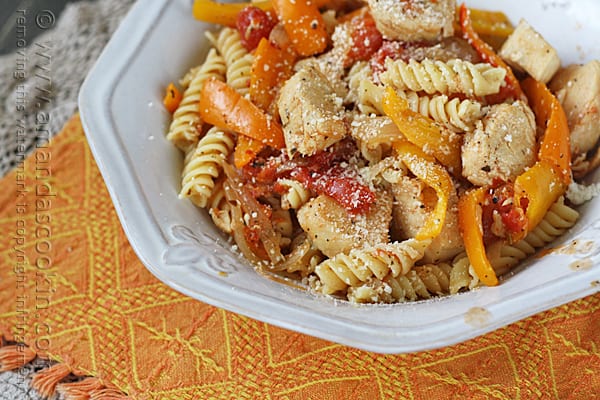 A close up photo of chicken with peppers and pasta in a white bowl topped with Parmesan cheese.