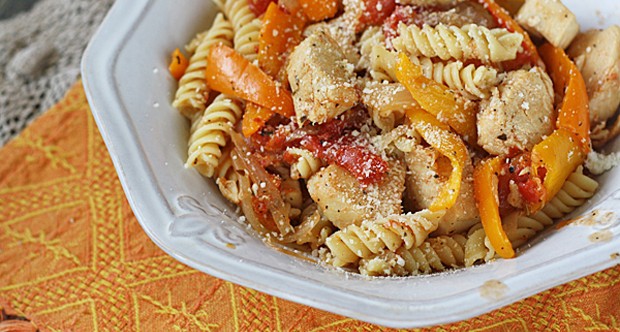 A close up photo of chicken with peppers and pasta in a white bowl topped with Parmesan cheese.