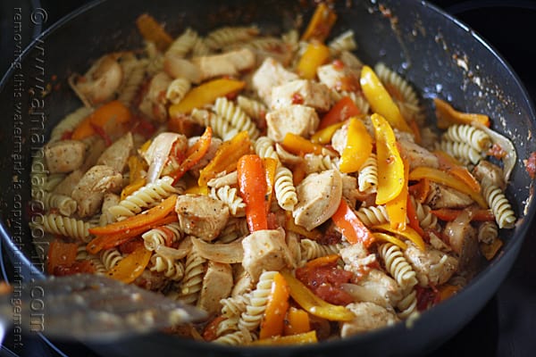 A close up photo of chicken with peppers and pasta in a skillet.