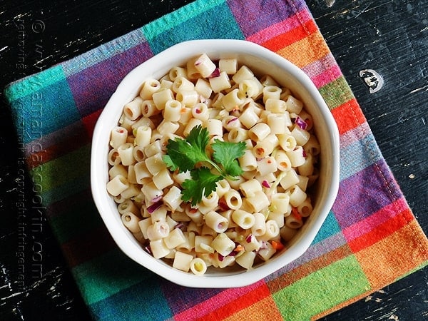 An overhead photo of pasta salad in a white bowl with parsley on top.