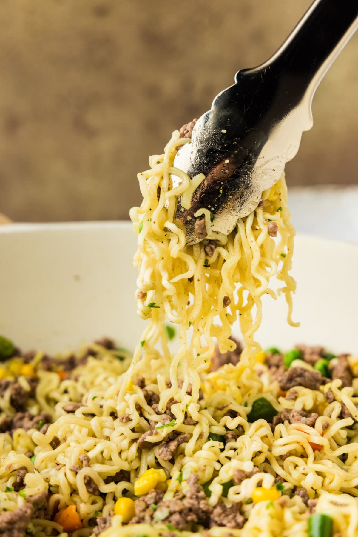 tongs lifting noodles from skillet