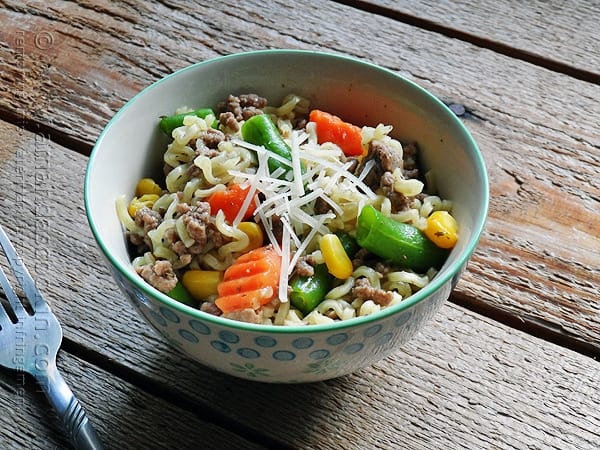 A photo of ramen noodle and beef skillet in a blue and white bowl.