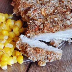 A close up photo of sliced pretzel chicken on a plate with corn.