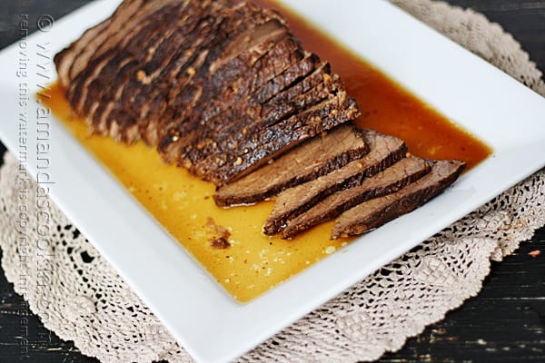 A close up of sliced slow cooker roast with brandy sauce on a white platter.