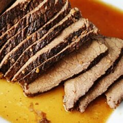 A close up of sliced slow cooker roast with brandy sauce on a white platter.