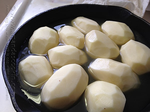 A close up photo of peeled potatoes in a cast iron skillet.