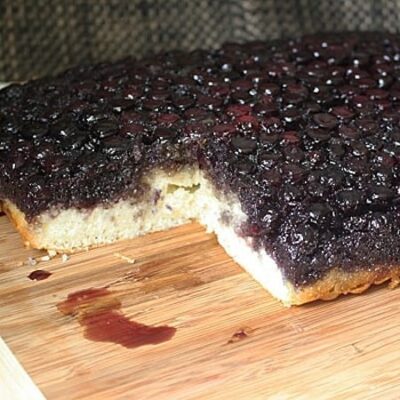A photo of an easy blueberry upside down cake resting on a wooden cutting board.