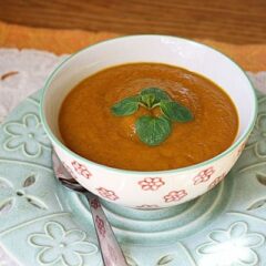 A close up photo of a bowl of pumpkin soup with a spoon on the side.