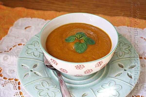 A close up photo of a bowl of pumpkin soup with a spoon on the side.