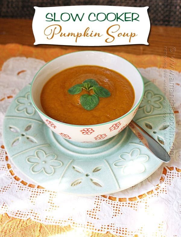 A close up photo of a bowl of pumpkin soup with a spoon on the side.