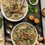 Two bowls of sausage mushroom wild rice soup on a dark metal tray with crusty bread, chopped parsley and whole mushrooms
