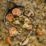 A ladle lifting sliced sausage, mushrooms and wild rice out of a pot of soup