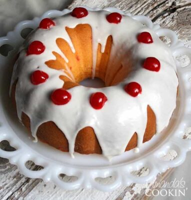 A close up photo of a maraschino cherry bundt cake with icing and cherries on top.
