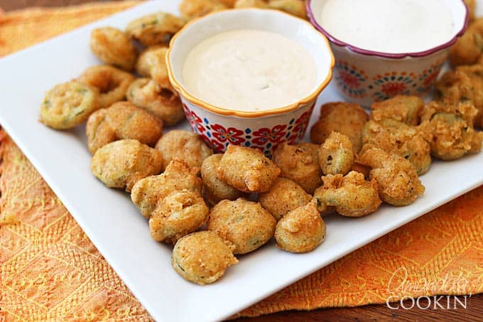 A plate of crispy fried jalapeno slices served with dipping sauce.