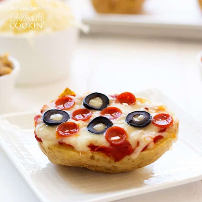 A close up of a baked potato pizza on  white plate topped with pepperoni and black olives.