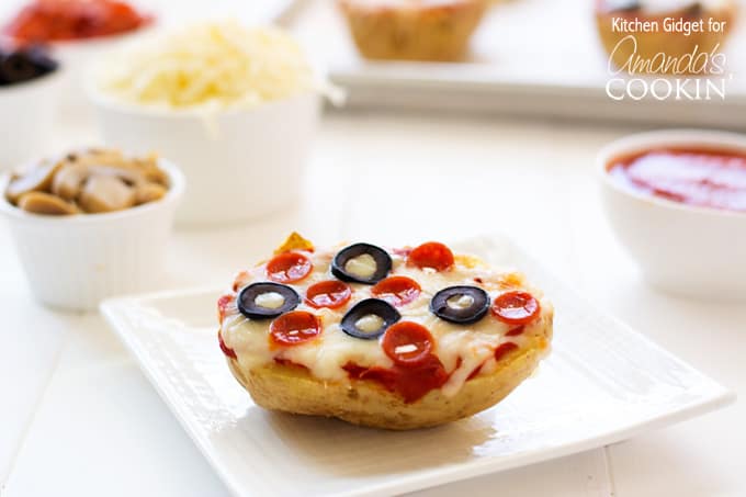 A close up of a baked potato pizza on  white plate topped with pepperoni and black olives.