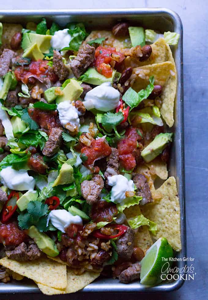 An overhead photo of filet mignon steak nachos topped with beans, rice, lettuce, avocado, salsa, sour cream, and cilantro.