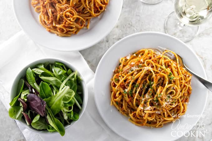 An overhead photo of two plated of sun dried tomato pesto on pasta with a salad on the side.