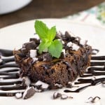 A close up photo of a peppermint patty brownie topped with drizzled chocolate sauce and a mint leaf.