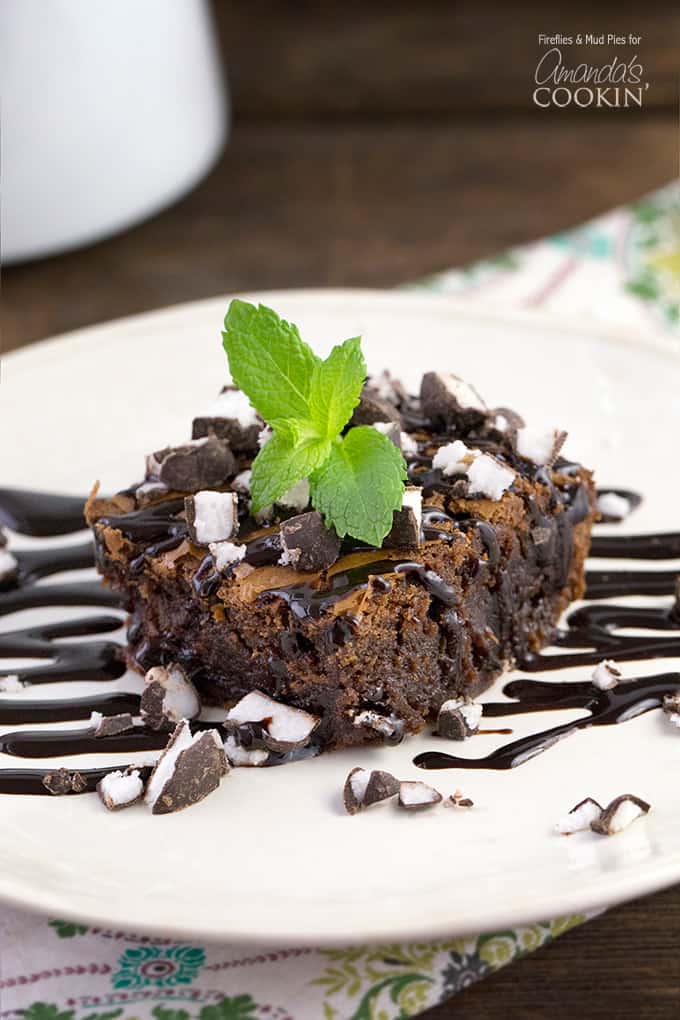 A close up photo of a peppermint patty brownie topped with drizzled chocolate sauce and a mint leaf.