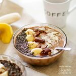 A close up of a mocha smoothie bowl topped with sliced banana, shaved chocolate and sliced almonds.