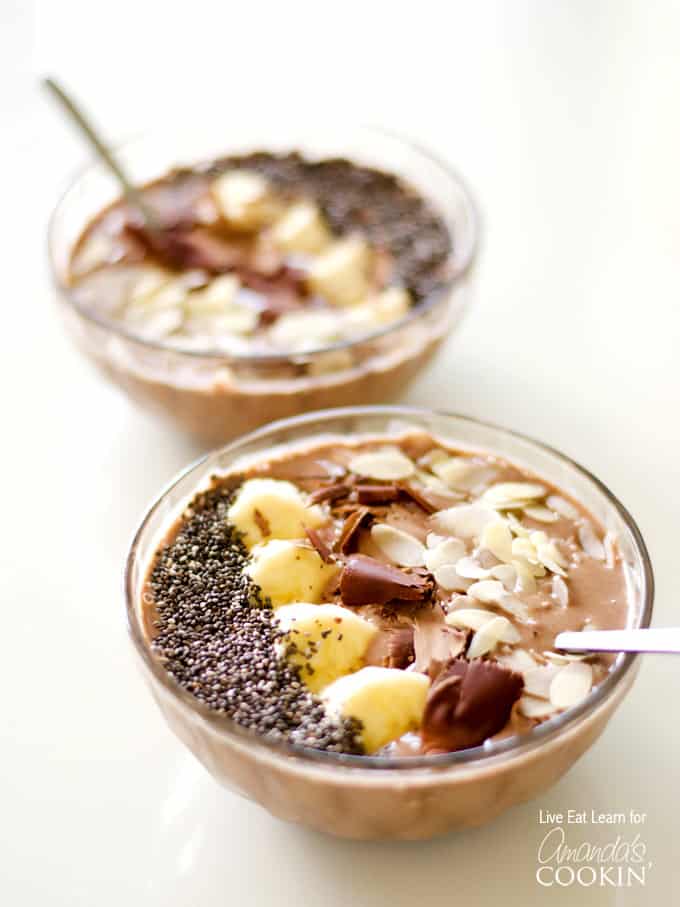 A close up of two mocha smoothie bowls topped with sliced banana, shaved chocolate and sliced almonds.