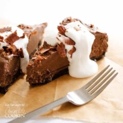 A close up of a slice of avocado chocolate mousse cake on a wooden cutting board with a fork next to it.