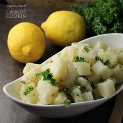 A close up of a long white bowl filled with Mediterranean potato salad and topped with chopped parsley.