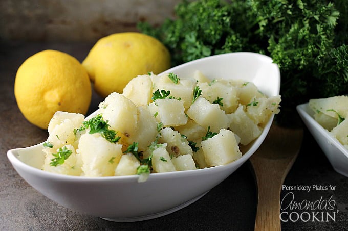 A white long bowl filled with Mediterranean potato salad topped with chopped parsley. 