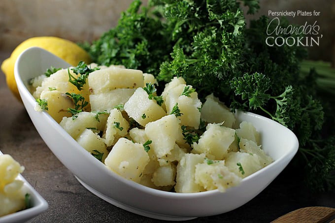 A close up of a long white bowl filled with Mediterranean potato salad and topped with chopped parsley.