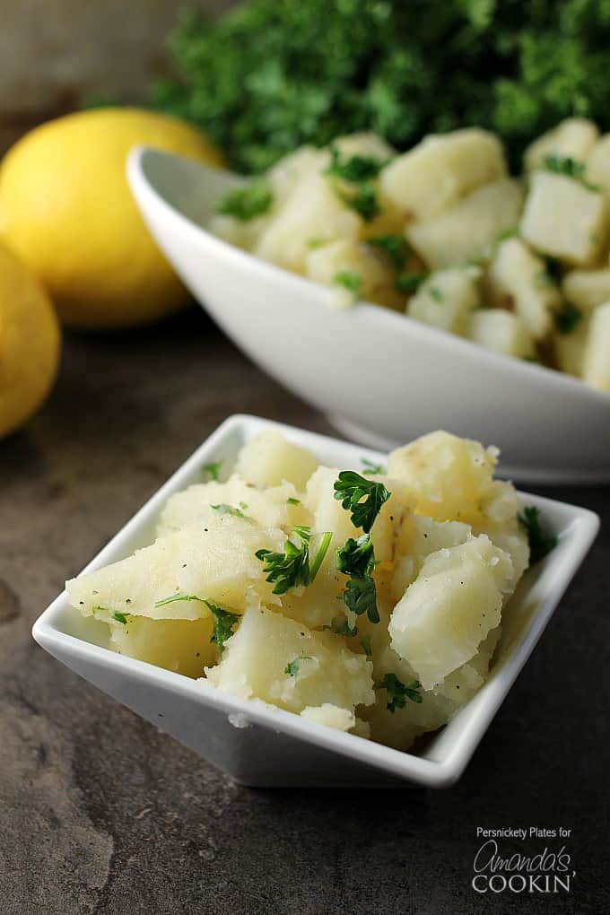 A close up of a small white bowl filled with Mediterranean potato salad and topped with chopped parsley.