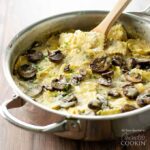 A saute pan filled with creamy mushroom ravioli and a wooden spoon.