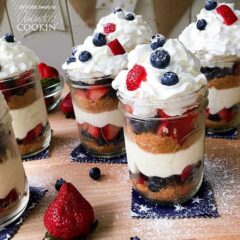 A close up of no bake berry cheesecake trifles in mason jars on a wooden cutting board.