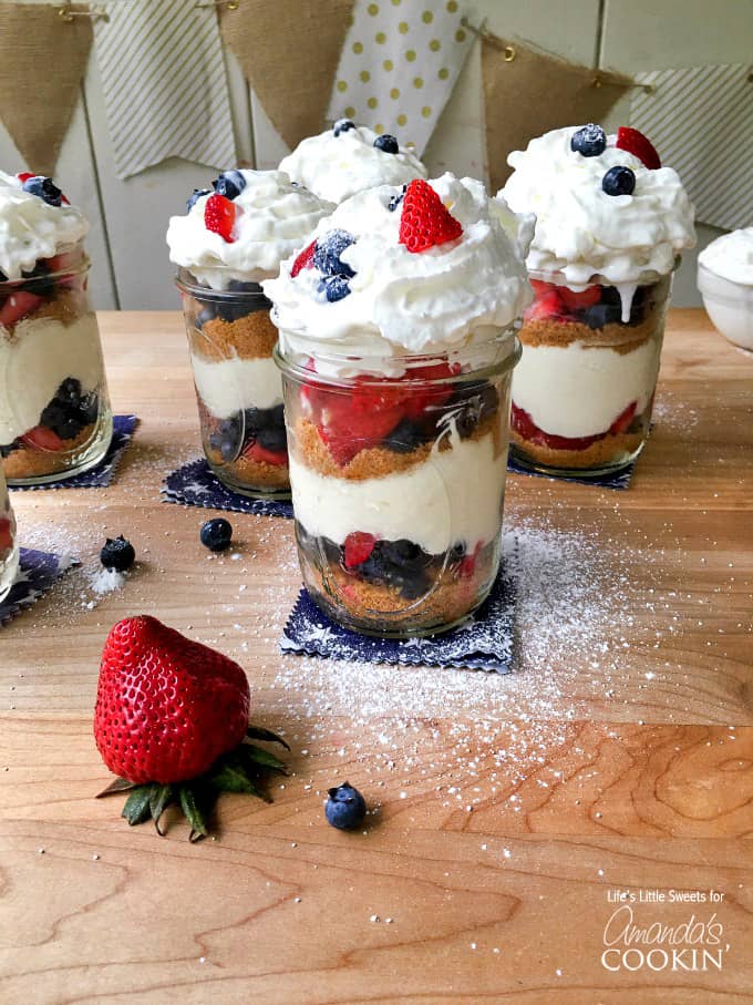 A close up of no bake berry cheesecake trifles in mason jars on a wooden cutting board.