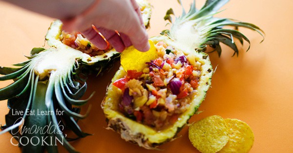 hand dipping chip into pineapple salsa