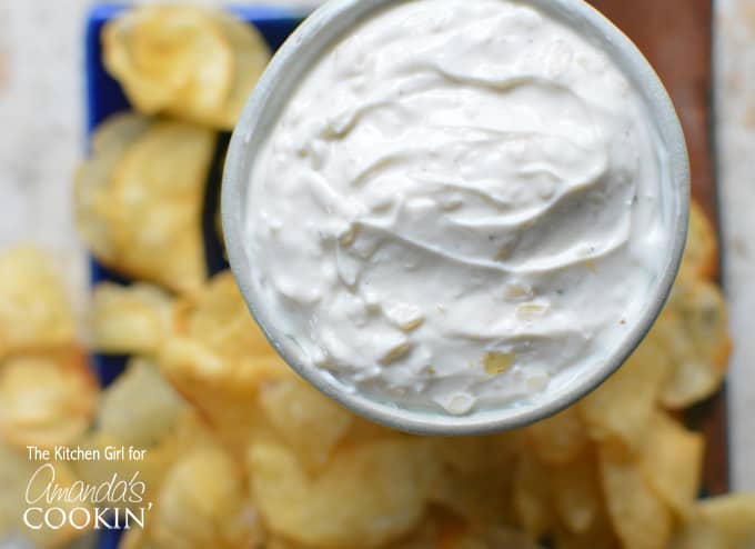 A close up overhead of skinny French onion dip in a white bowl with potato chips in the background.