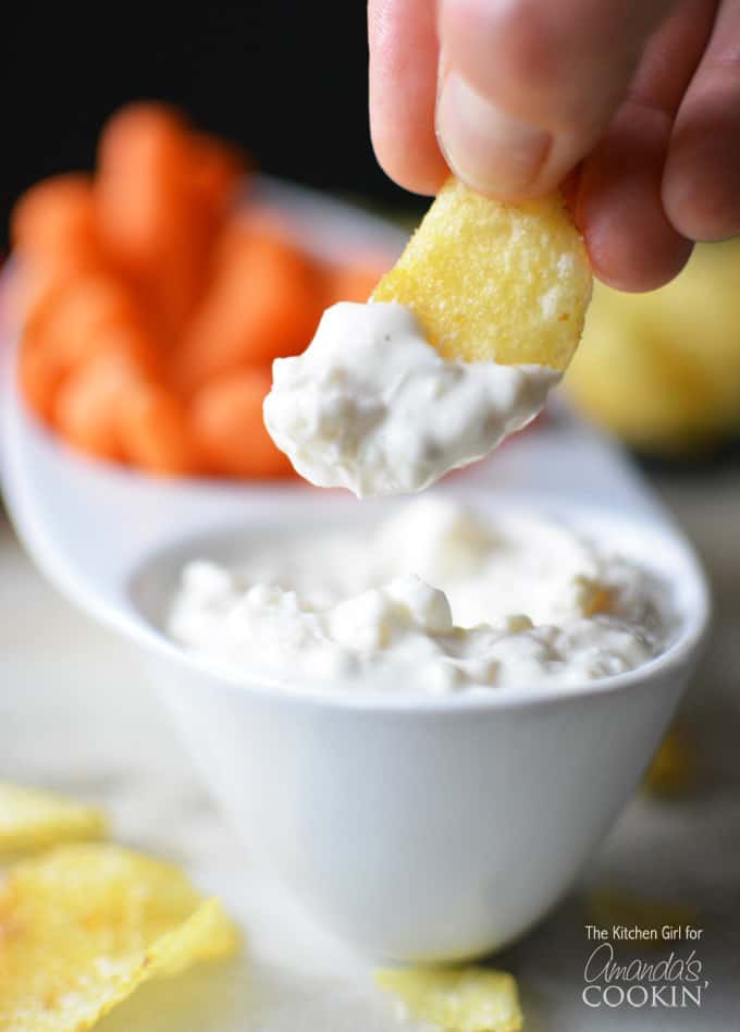 A close up of a potato chip with skinny French onion dip on it and the bowl of dip in the background.