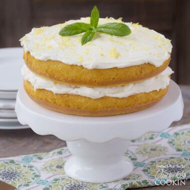 A close up of a lemon curd poke cake on a white cake stand topped with fresh mint leaves.
