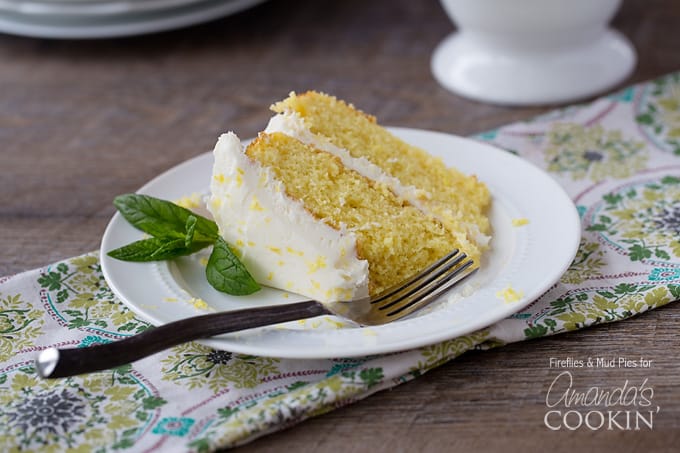 A close up of a slice of lemon curd poke cake on a white plate with fresh mint leaves on the side.