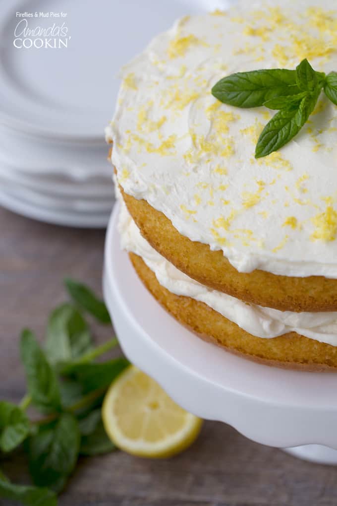 A close up of a lemon curd poke cake on a white cake stand topped with fresh mint leaves.