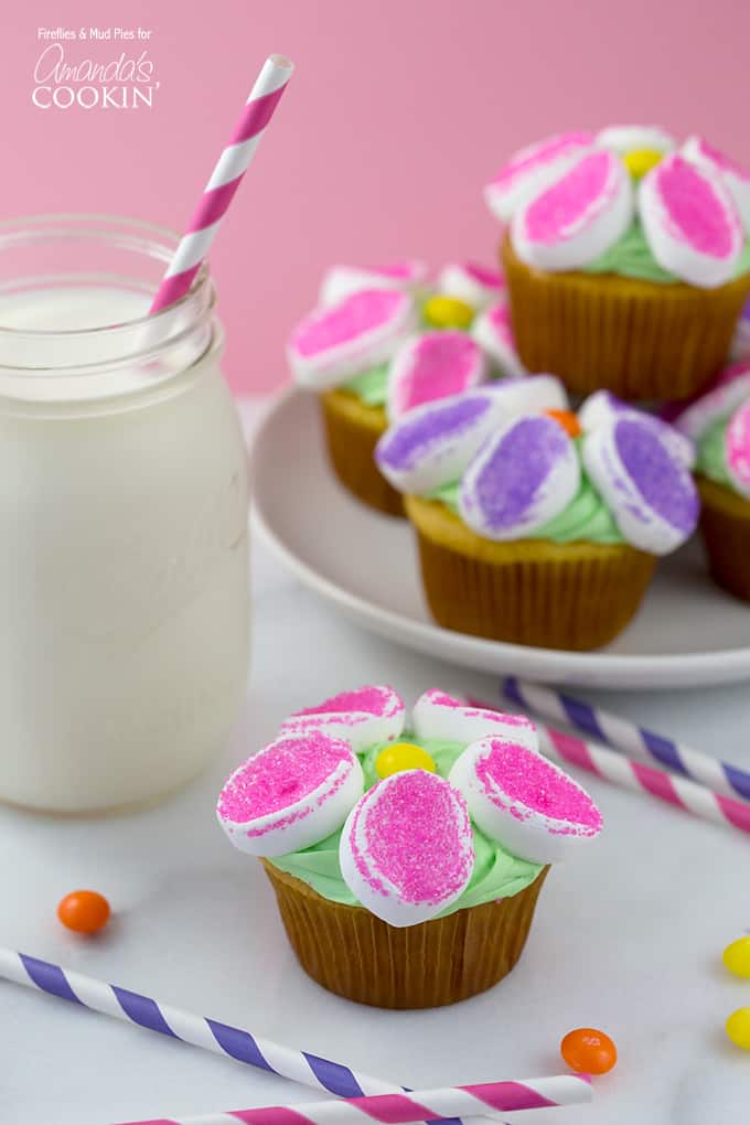 A photo of marshmallow flower cupcakes with a glass of milk to the side.