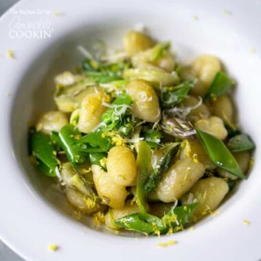 A close up overhead photo of pan seared gnocchi with shaved asparagus and snap peas in a white bowl.