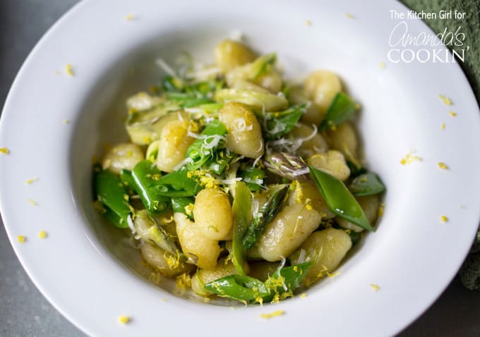 A close up overhead photo of pan seared gnocchi with shaved asparagus and snap peas in a white bowl.